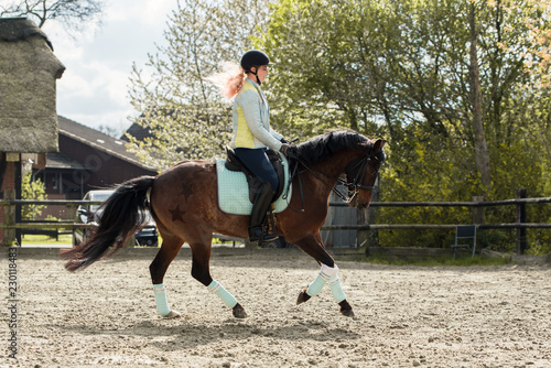 Reiterin galopiert in Pastelfarben mit ihrem Pony über einen Reitplatz