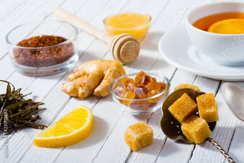 cup of tea, different leaves, honey, lemon ginger and brown sugar on white wooden table background