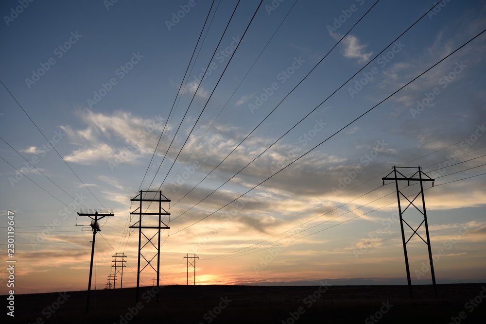 Power grid distribution network silhouette, electrical transmission pylon and high voltage power lines passing into the distant horizon at sunset