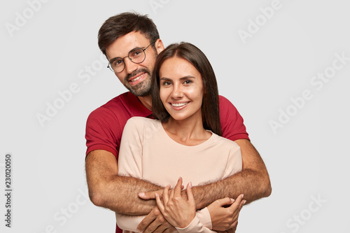 Lovely couple have warm cuddle, pose for family portrait, smile joyfully, have good relationships. Affectionate brother embraces his sister isolated over white wall. Girlfriend and boyfriend have date