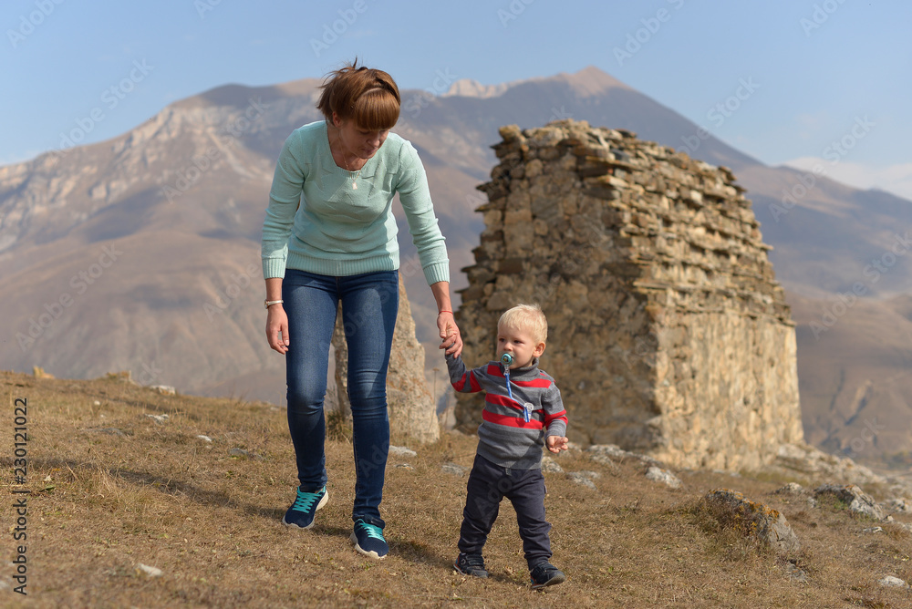 A little boy with a pacifier travels with his mother, walking among the ancient Ossetian buildings in North Ossetia - Alania.