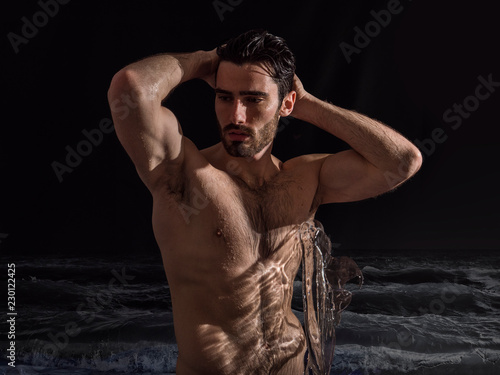 Handsome shirtless young man outdoor at night bathing in sea or ocean, with ripped fit body