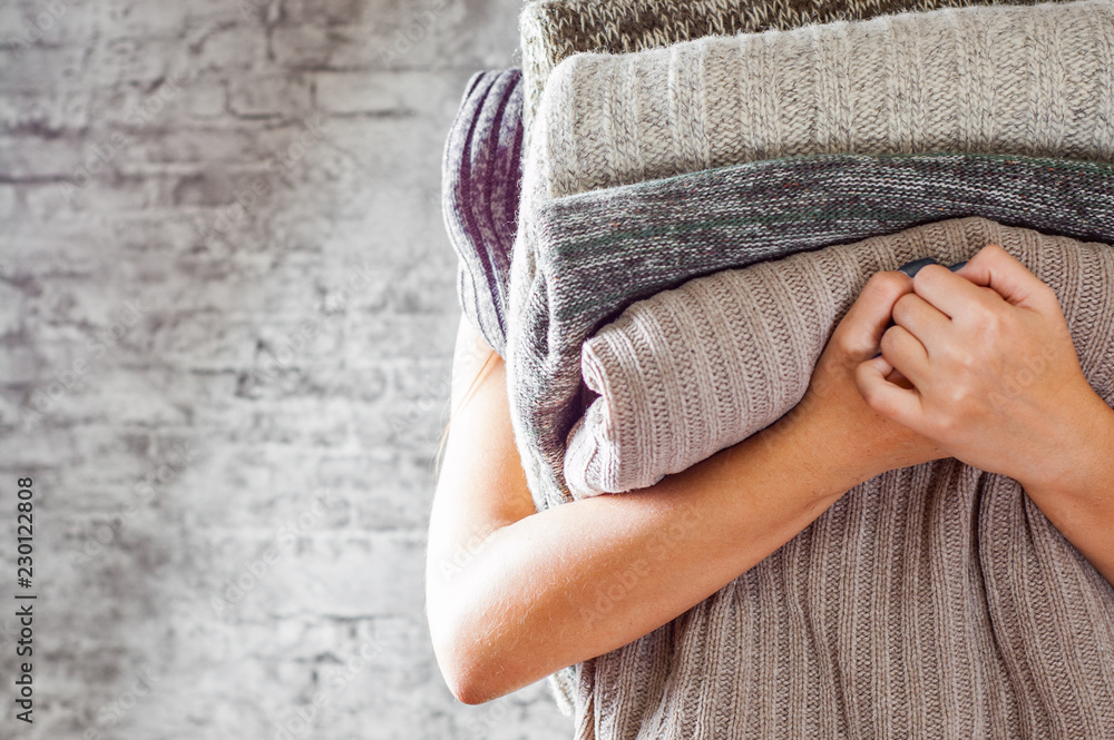 woman holding in hands Stack of cozy knitted sweaters on gray wall background - obrazy, fototapety, plakaty 