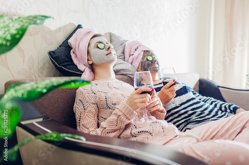 Mother and her adult daughter applied facial masks and cucumbers on eyes. Women chilling while having wine photo