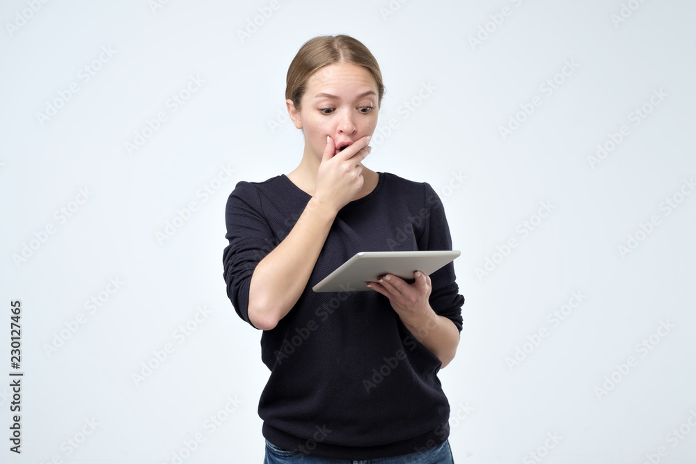 Shocked woman looking at digital tablet with surprise and shock over gray background. Astonishment or hot news in internet Shocked woman looking at digital tablet with surprise and shock over gray background. Astonishment or hot news in internet