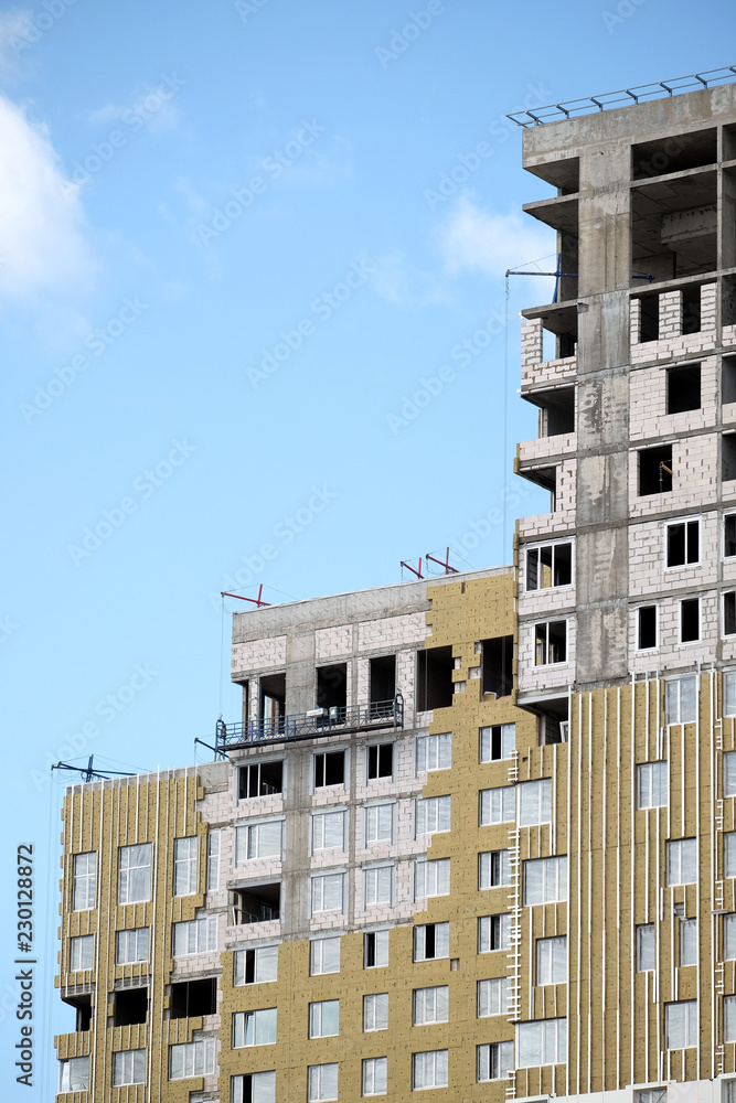 Process of mounting insulation on apartment building facade in new modern urban house over blue sky with clouds closeup
