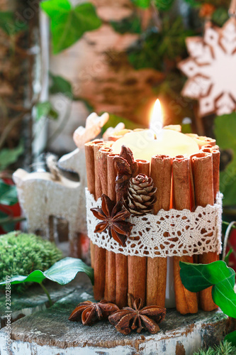 Candle decorated with cinnamon sticks, moss, ivy leaves and wooden deers