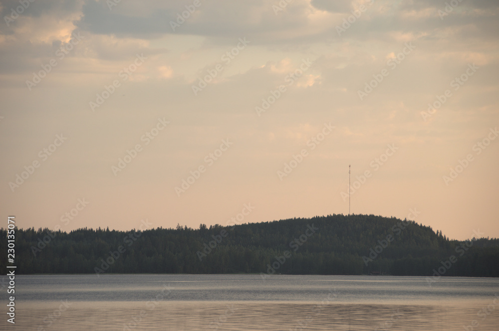 Golden hour an einem Finnischen See mit schattigen Hügeln im Hintergrund.