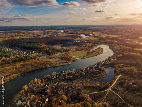 Aerial view of rural landscape in autumn sunset. Small village houses, river, autumn trees, farm fields from drone point of view