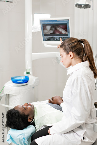Charming beautiful girl doctor dentist. Young African American male patient at chair at dental clinic. Medicine  health  stomatology concept. dentist conducts inspection and concludes