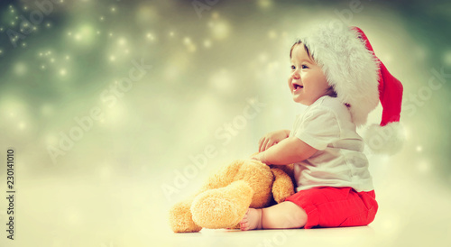 Toddler boy with santa hat playing with his teddy bear in snowy night