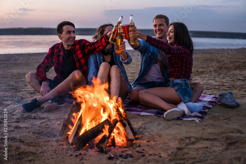 Camp on the beach. Group of young friends having picnic with bonfire. They drink beer