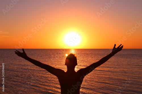 A young man with his arms outstretched is watching the sunset on the seashore. Background. Landscape. © far700