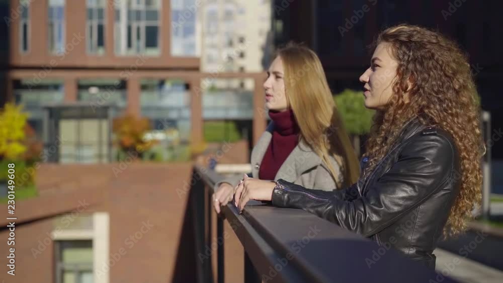 Side view shot of two female best friends lean on handrails and talking, friends spending time together. Side view shot of two female best friends lean on handrails and talking, friends spending time together.