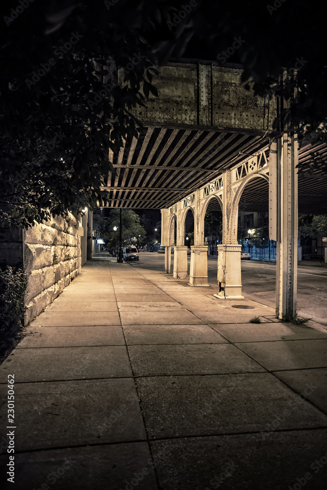 City street sidewalk and alley at night under a vintage train bridge