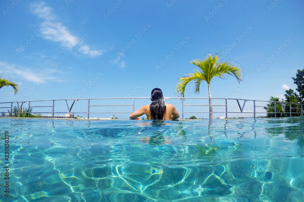 Girl in resort style infinity swimming pool overlooking Seminyak, Bali, Indonesia.