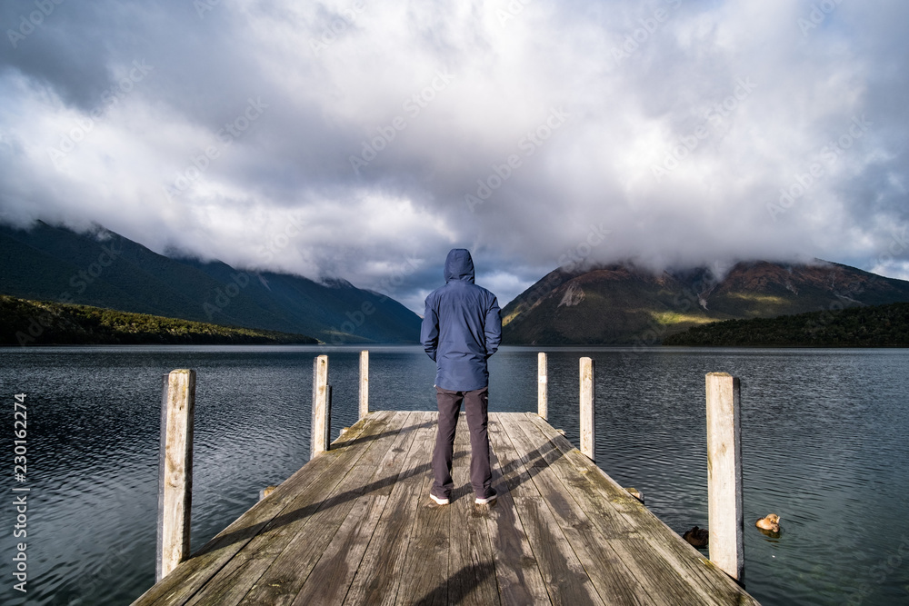 A man with blue jacket standing on dock enjoying with a view of lake Rotoiti, Nelsonlake National Park, New Zealand.