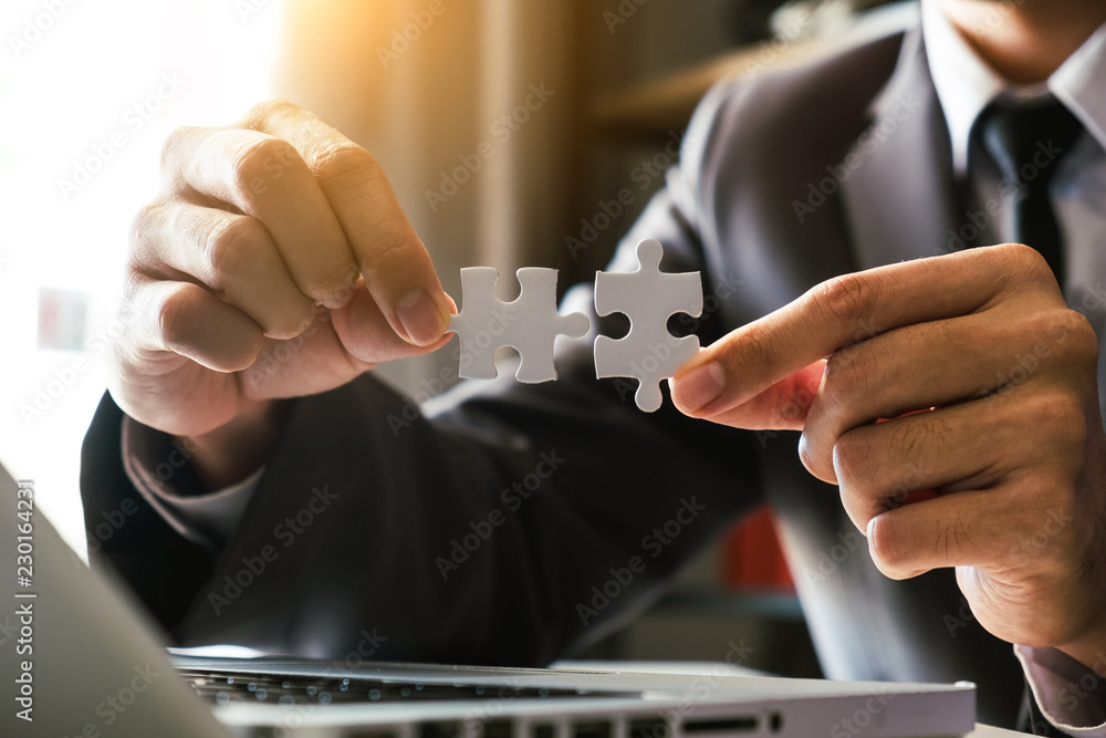 Naklejka premium Business solutions and success concept. Businessman hand connecting jigsaw puzzle at office in morning light