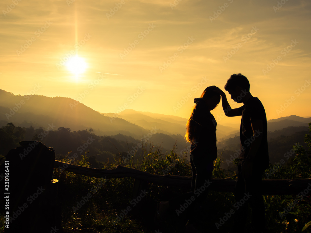 Silhouette of happy young couple in love looking view sunset on the mountain. Pat on the Head