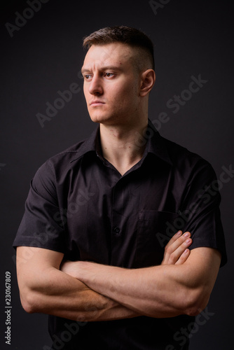 Young handsome businessman with arms crossed against gray background