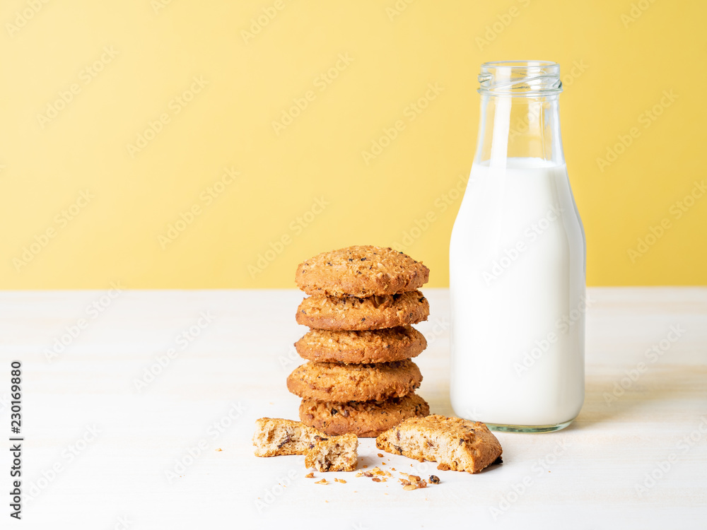 Oatmeal cookies with flax seeds and milk in bottle, healthy snack. Light background, bright yellow wall