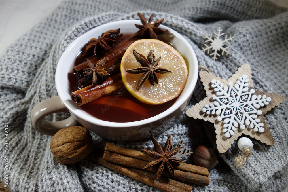 Fototapeta premium A hot drink with spices wrapped in a woolen shawl. Selective focus.Still life, food and drink, seasonal and holidays