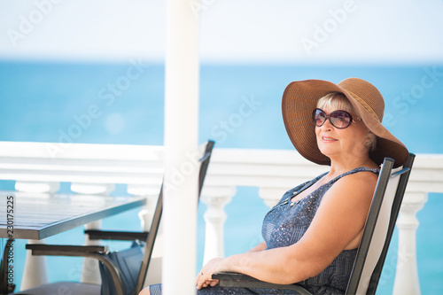 An elderly woman sitting in the outdoor restaurant, sea at the background