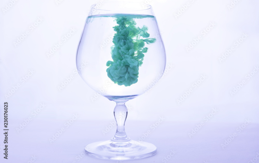 green paint in water in a crystal glass on a white background green paint in water in a crystal glass on a white background