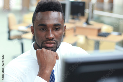 Portrait of successful African-American businessman sitting at desk with computer in office.