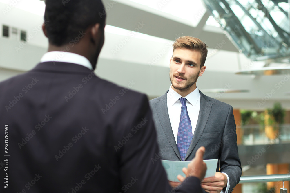 Two multinational young businessmen discussing business at meeting in office. Two multinational young businessmen discussing business at meeting in office.
