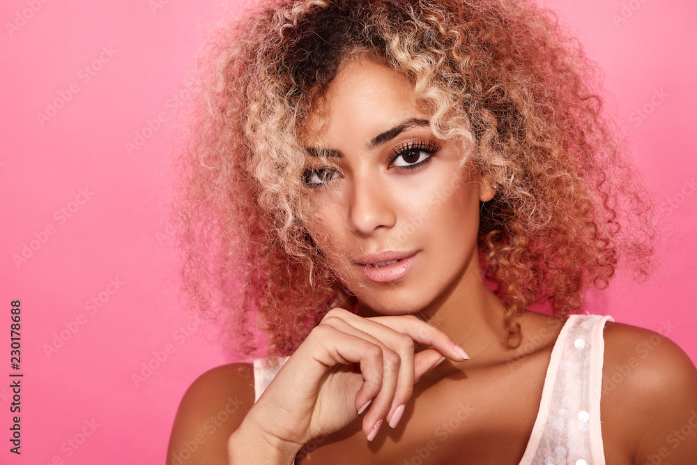 Fototapeta premium Portrait of blissful lovable woman with blond african hairstyle. Smiling model girl in trendy summer clothes posing on pink background