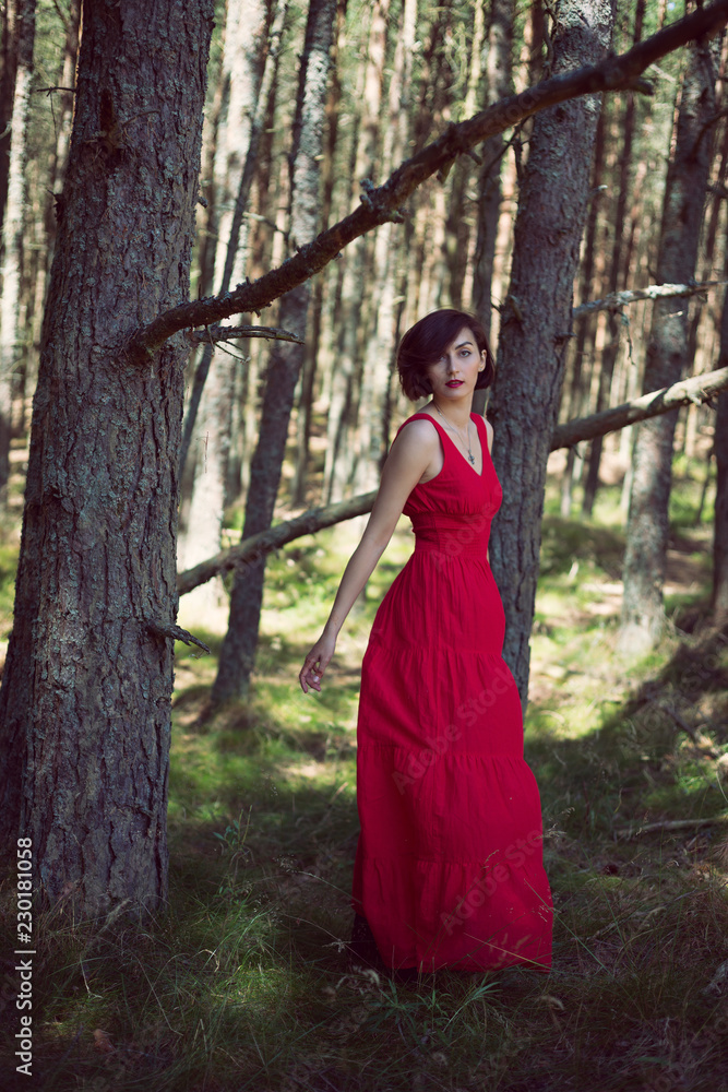 Young brunette woman in red dress walking in the forest Young brunette woman in red dress walking in the forest
