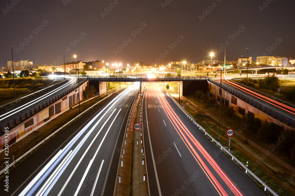 DIFFERENT TRAFFIC LIGHTS OF VEHICLES IN A MOTORWAY WITH THE LIGHTS OF THE CITY AT THE END