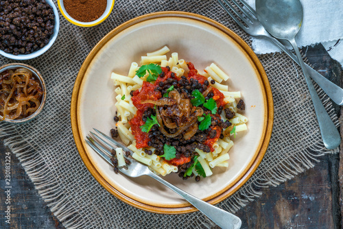 Kushari - Egyptian vegetarian dish with lentils, spiced tomato sauce and macaroni topped with fried onions - top view photo