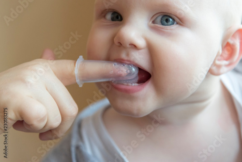 Mom brushes baby's teeth with a brush that fits on her finger