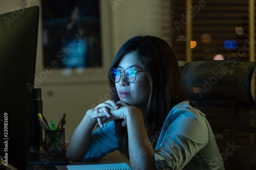 Obraz na płótnie Portrait of Asian Businesswoman working hard and looking the digital graphic on the table with front of computer desktop in workplace at late with serious action, Work hard and too late concept w salonie