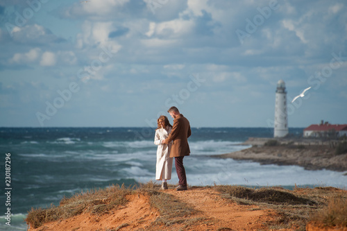 fashionable couple in coats young man and woman on stormy sea coast with white beacon © ruslanshug