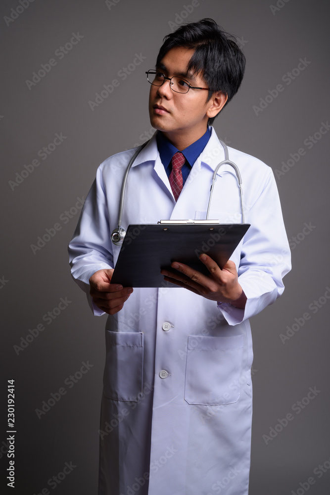 Portrait of young Asian man doctor holding clipboard and thinking Portrait of young Asian man doctor holding clipboard and thinking