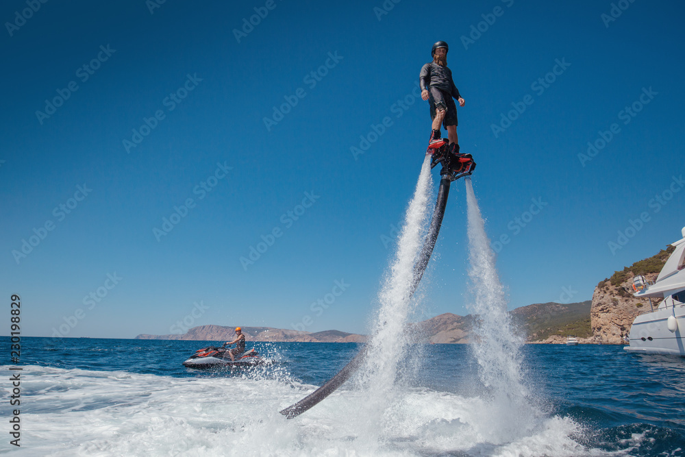 Flyboarding and seariding on the Sea near the mountain island. Water summer extreme sports. - obrazy, fototapety, plakaty 