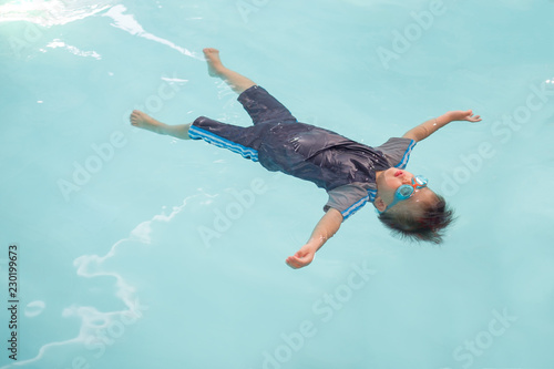 Cute little Asian 30 months / 2 years old toddler baby boy learn to swim in swimming class in Thailand, Kid learn to float (back floating) at indoor salt water pool, Beginner Swimmers concept