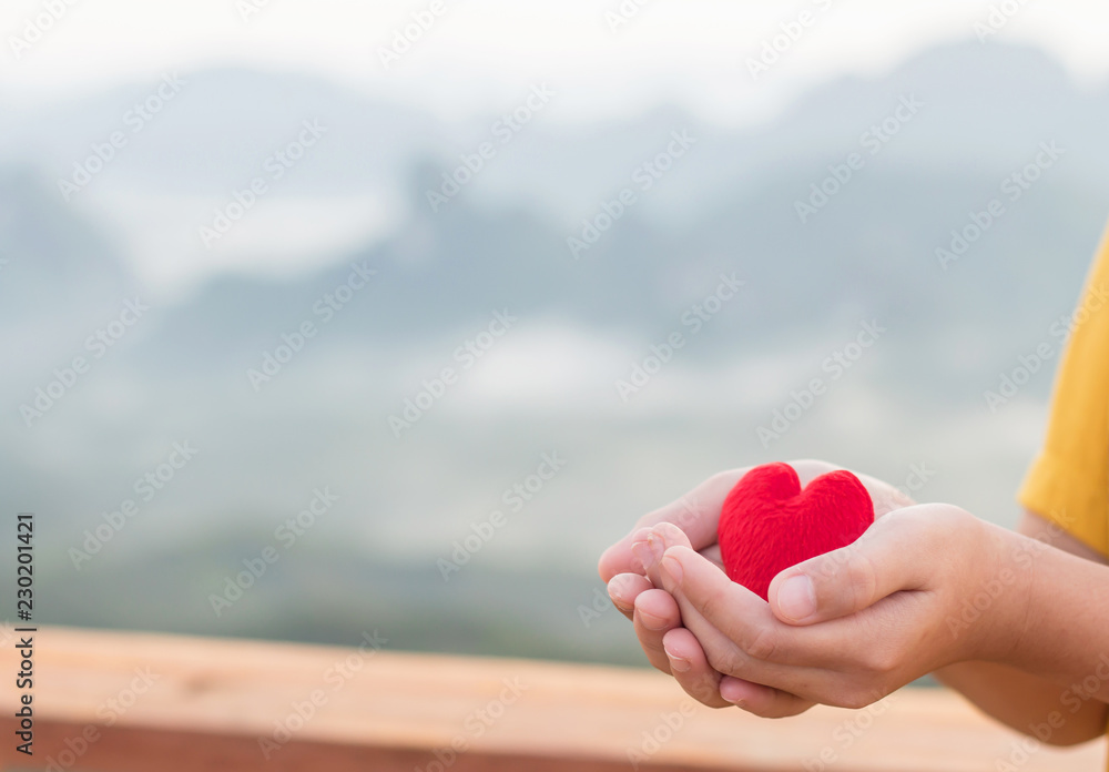 Fototapeta premium Hand boy holds the red heart with mountains landscape. copy space for text. the concept of love, Valentines day, symbol and romantic. red heart for gift.