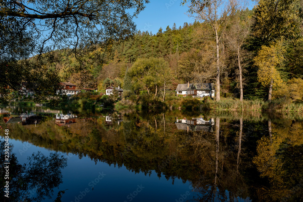 Fototapeta premium houses and trees on the banks of the river, reflecting on the surface in autumn