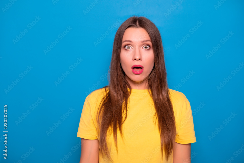 Cute brunette woman with long hair posing in yellow t-shirt on a blue background. Emotional portrait. She shocked, amazed Cute brunette woman with long hair posing in yellow t-shirt on a blue background. Emotional portrait. She shocked, amazed