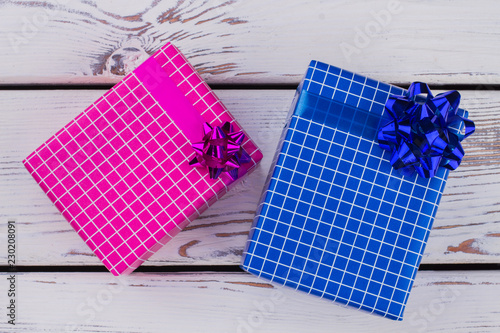 Pink and blue gift boxes on wooden background. Top view on two square gift boxes on white wooden boards. Holiday greeting gifts.