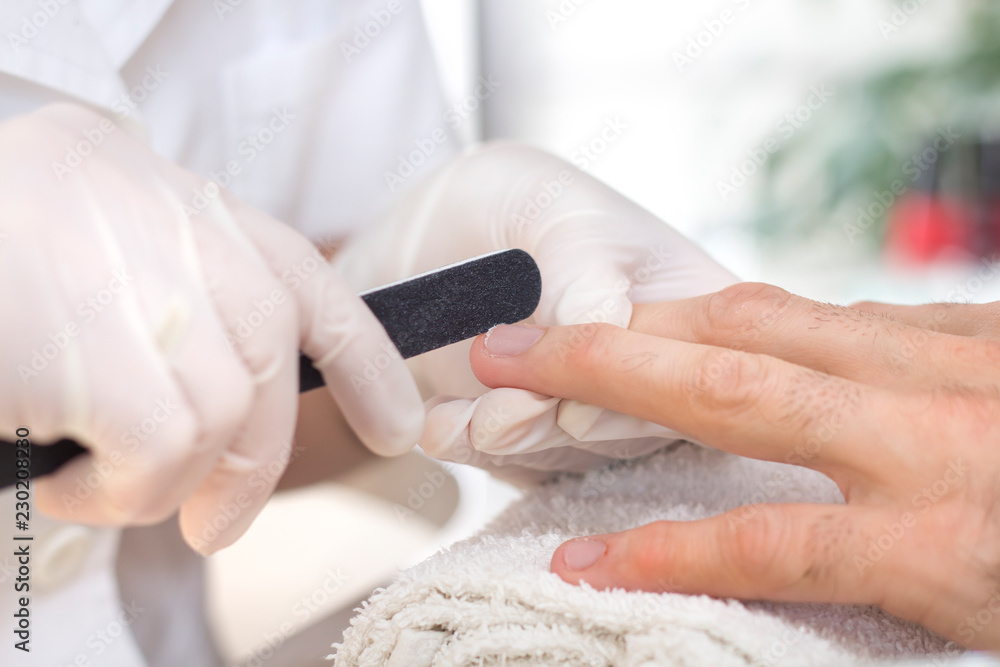 Dłonie kosmetyczki w gumowych rękawiczkach piłują paznokcie w męskiej dłoni podczas zabiegu manicure.