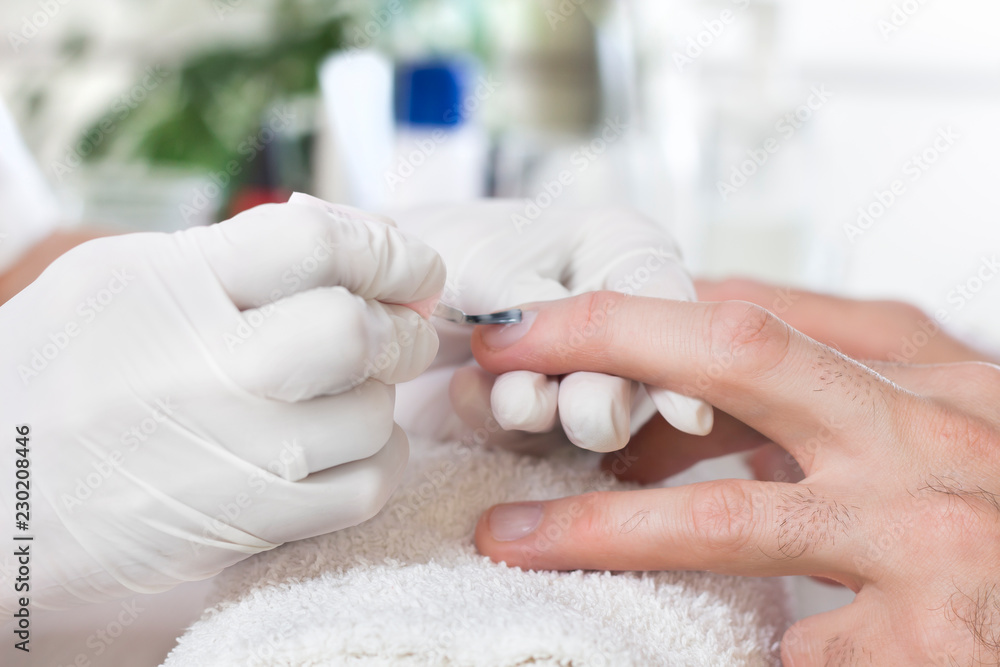 Męska pielęgnacja manicure. Kosmetyczka nakłada odżywkę na paznokcie mężczyzny.
