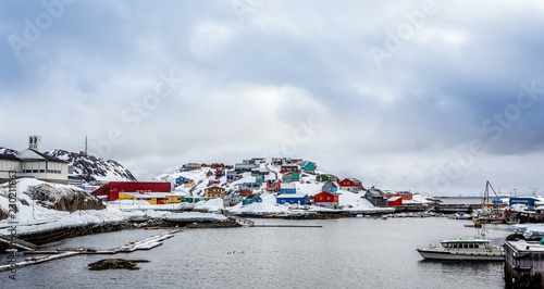 Port with boats and colorful Inuit houses on the rocks in backgr