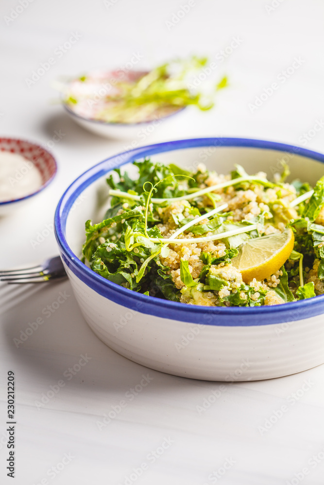 Kale, quinoa, avocado vegan salad in a white bowl on a white background.
