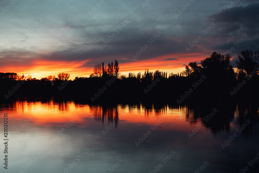 Colorful calm summer lake sunset with long exposure clouds and textured sky and tree silhouettes. Südsee in Braunschweig, Germany