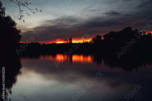 Dramatic long exposure of a calm lake with blurry clouds and sunset light and tree reflection. S  dsee in Braunschweig  Germany